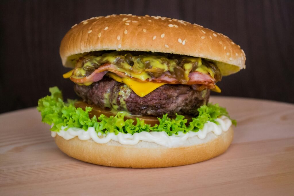 Close-up of a delicious cheeseburger with lettuce, mayo, and toppings on a wooden surface.